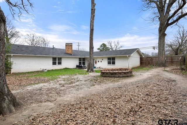 back of property featuring driveway, brick siding, fence, and a chimney