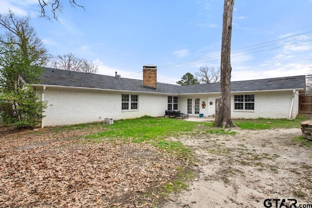 back of property with a patio, brick siding, a chimney, and a lawn