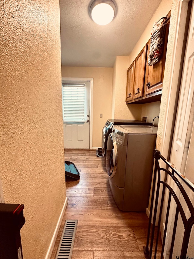 washroom featuring a textured ceiling, light wood-type flooring, washer and clothes dryer, and cabinets