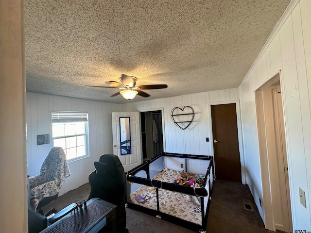 carpeted bedroom featuring wood walls, a textured ceiling, and ceiling fan