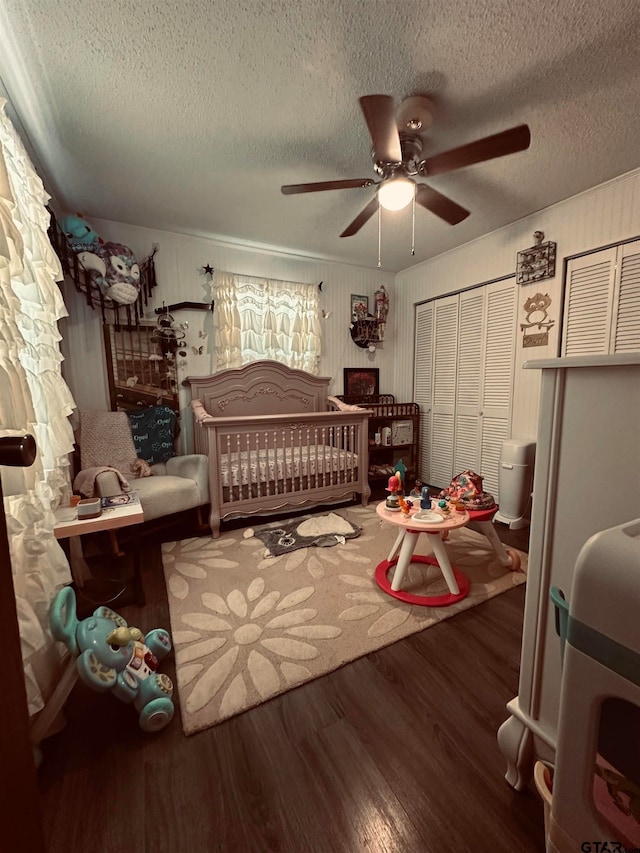 bedroom featuring a nursery area, a textured ceiling, hardwood / wood-style flooring, and ceiling fan