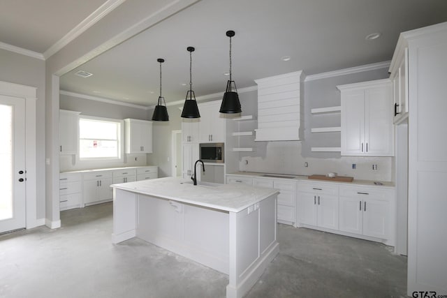 kitchen featuring white cabinetry, crown molding, stainless steel microwave, an island with sink, and light stone countertops