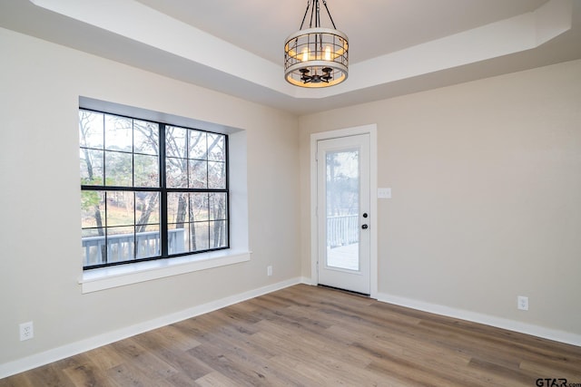 interior space with a wealth of natural light, wood-type flooring, a tray ceiling, and a notable chandelier