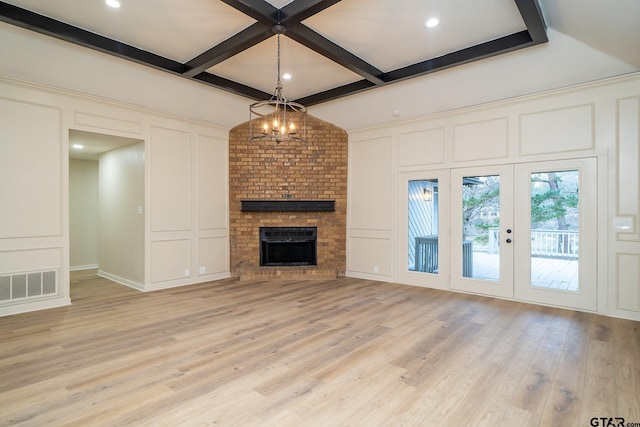 unfurnished living room with beam ceiling, coffered ceiling, a brick fireplace, light wood-type flooring, and french doors