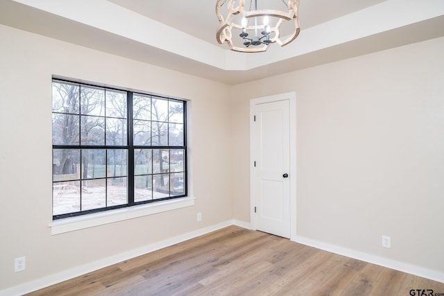 unfurnished room featuring a chandelier, light hardwood / wood-style floors, and a raised ceiling