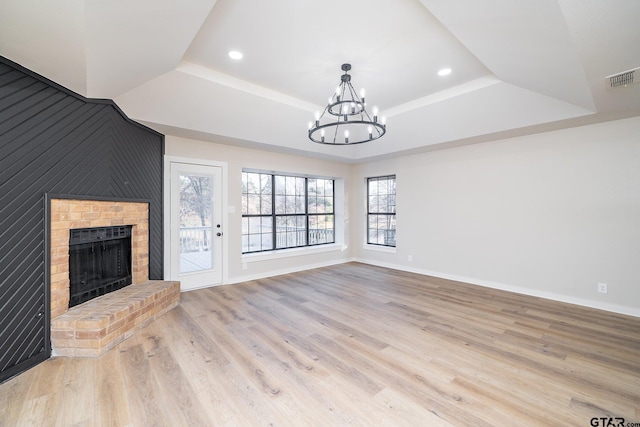 unfurnished living room with a tray ceiling, an inviting chandelier, a brick fireplace, and light hardwood / wood-style flooring