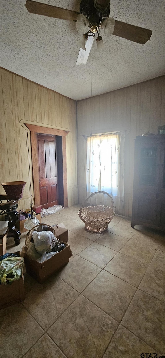 interior space featuring a ceiling fan, tile patterned flooring, wood walls, and a textured ceiling