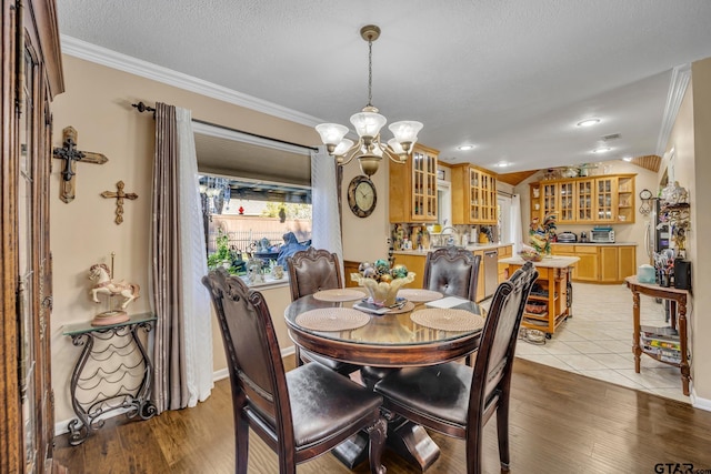 dining room featuring light hardwood / wood-style flooring, a notable chandelier, a textured ceiling, indoor bar, and ornamental molding