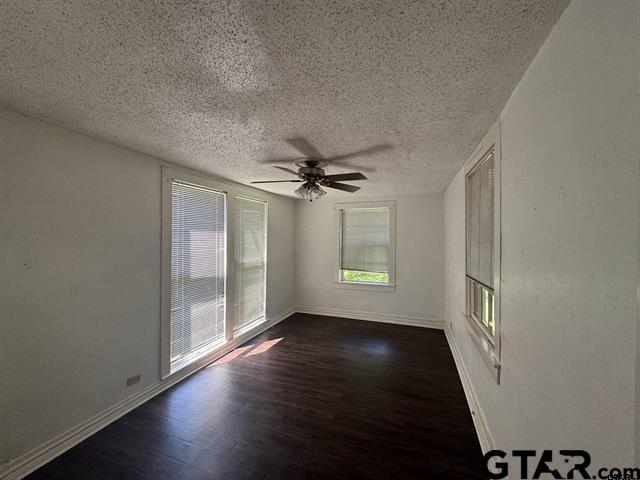 spare room with a textured ceiling, ceiling fan, and dark wood-type flooring