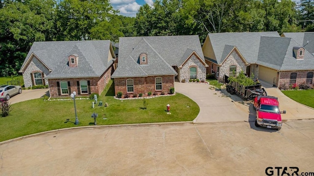 1216 Cobblestone Ct, Carthage, TX 75633 - french country style house with concrete driveway, brick siding, and a front yard