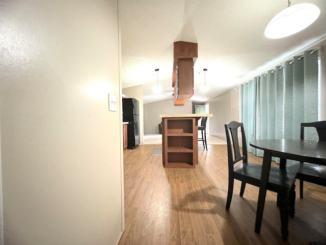 dining room with light hardwood / wood-style floors, a textured ceiling, and vaulted ceiling