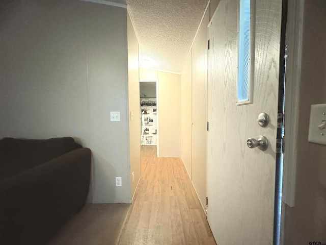 corridor featuring light wood-type flooring, a textured ceiling, and vaulted ceiling