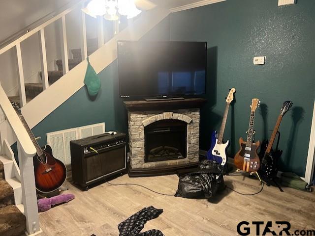 living area with stairs, a ceiling fan, wood finished floors, and a stone fireplace