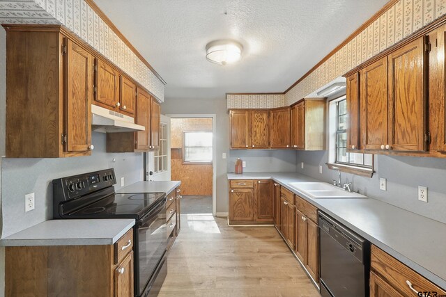 kitchen with brown cabinets, under cabinet range hood, a sink, light wood-type flooring, and black appliances