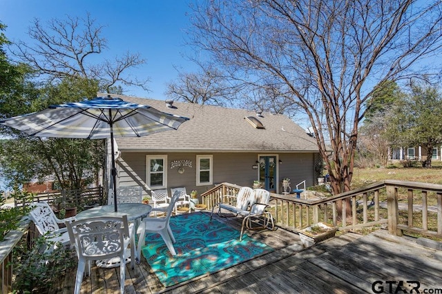 rear view of property with a deck, outdoor dining space, and roof with shingles