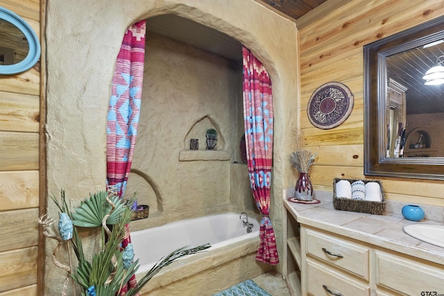 bathroom featuring tiled bath, wood walls, and vanity