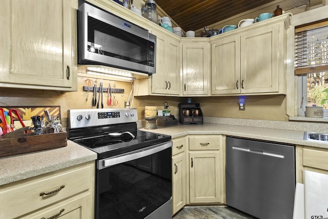 kitchen featuring vaulted ceiling, appliances with stainless steel finishes, light brown cabinetry, and light hardwood / wood-style flooring