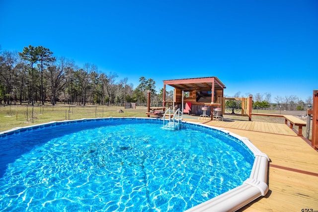 outdoor pool with fence, a lawn, and a wooden deck