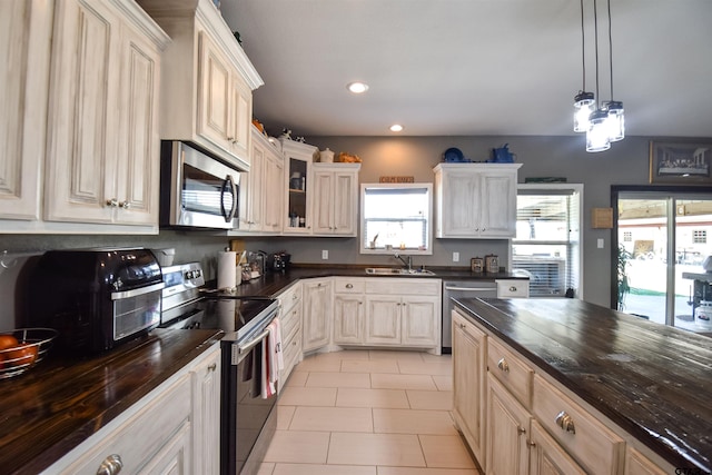 kitchen featuring light tile patterned floors, glass insert cabinets, appliances with stainless steel finishes, decorative light fixtures, and a sink