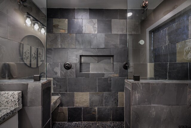 bathroom featuring tiled shower, vanity, and tile walls