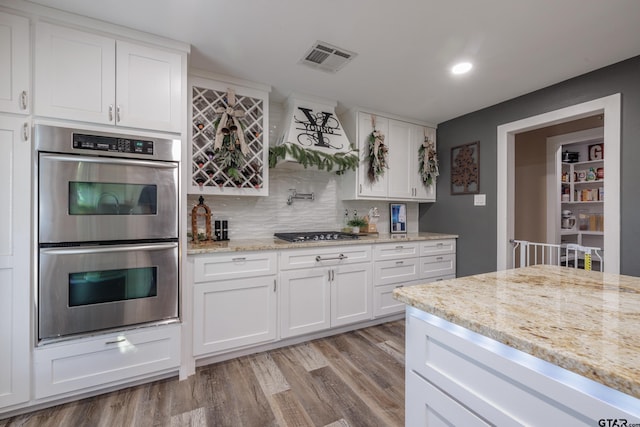 kitchen with backsplash, light wood-type flooring, appliances with stainless steel finishes, light stone counters, and white cabinetry