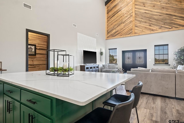 kitchen with a kitchen breakfast bar, light wood-type flooring, high vaulted ceiling, a center island, and green cabinets