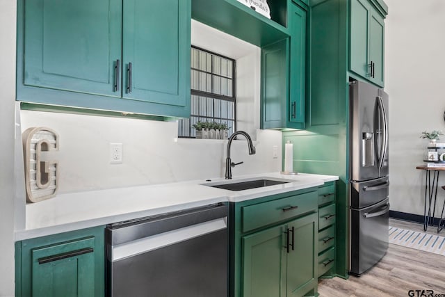 kitchen with green cabinets, sink, appliances with stainless steel finishes, and light hardwood / wood-style flooring