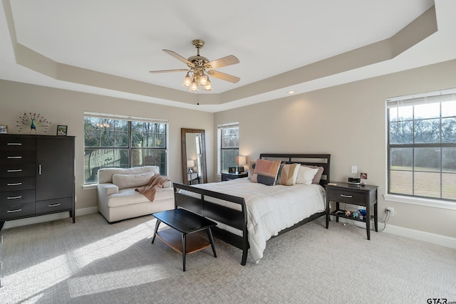 carpeted bedroom with multiple windows, a tray ceiling, and ceiling fan