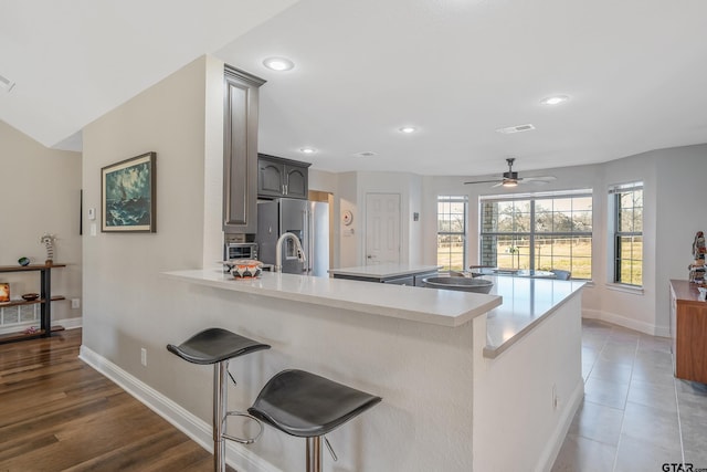 kitchen with kitchen peninsula, a kitchen breakfast bar, ceiling fan, dark wood-type flooring, and stainless steel fridge with ice dispenser