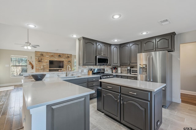 kitchen featuring kitchen peninsula, stainless steel appliances, sink, a center island, and gray cabinets