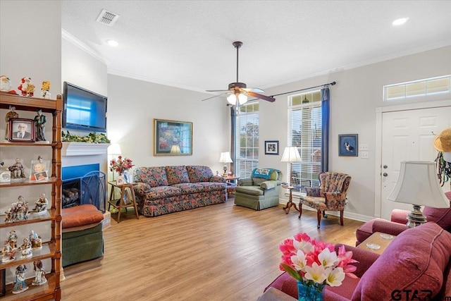 living room with ceiling fan, light hardwood / wood-style floors, ornamental molding, and a textured ceiling