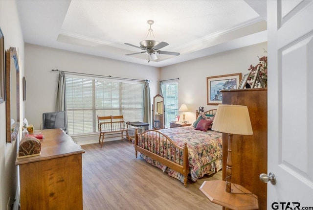 bedroom with ceiling fan, light wood-type flooring, and a tray ceiling