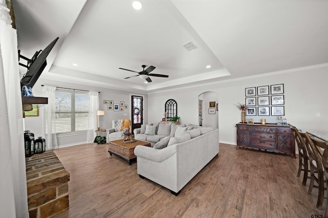 living room with a raised ceiling, ceiling fan, and wood-type flooring