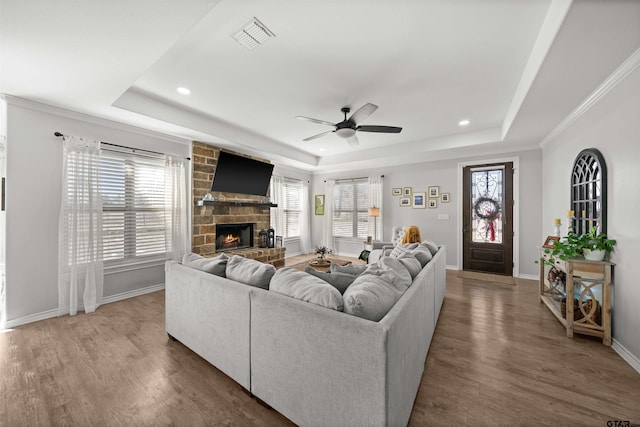 living room with a raised ceiling, ceiling fan, a fireplace, and wood-type flooring