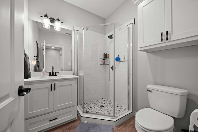 bathroom with hardwood / wood-style flooring, a shower with door, vanity, and toilet