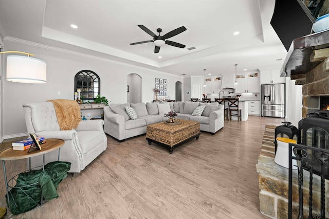 living room with a tray ceiling, light hardwood / wood-style flooring, ceiling fan, and crown molding