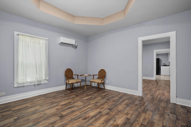 sitting room featuring an AC wall unit, baseboards, wood finished floors, and a tray ceiling