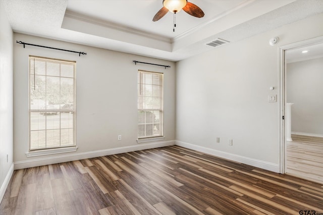 empty room with ceiling fan, a raised ceiling, ornamental molding, and dark wood-type flooring