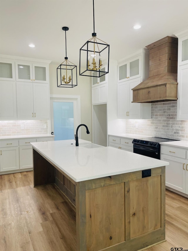 kitchen with white cabinetry, premium range hood, black electric range, a kitchen island with sink, and light wood-type flooring