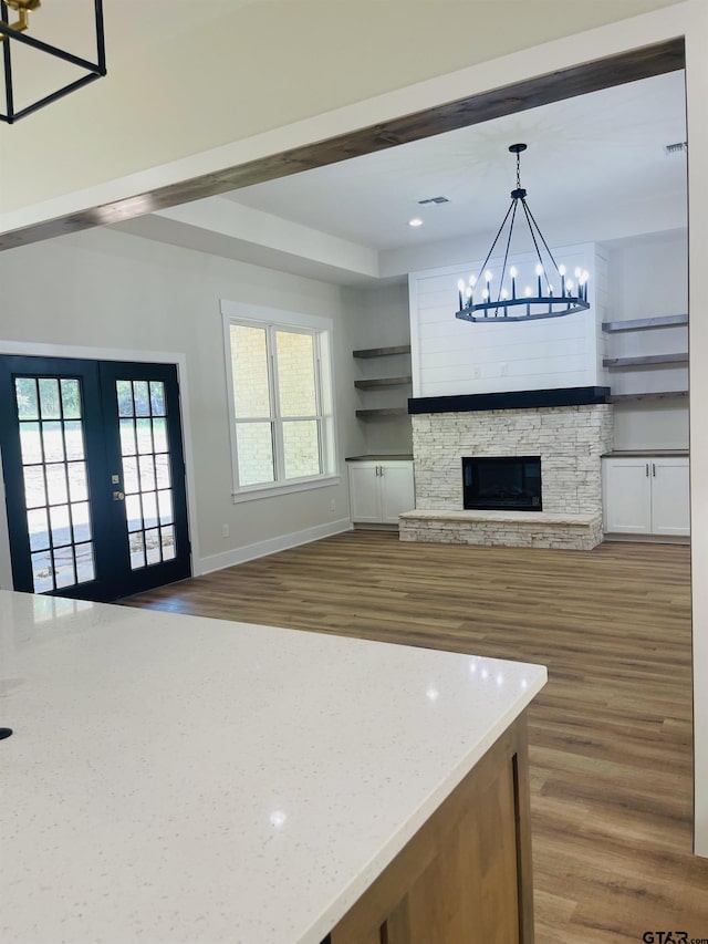 kitchen with a stone fireplace, light stone counters, hanging light fixtures, a chandelier, and hardwood / wood-style flooring