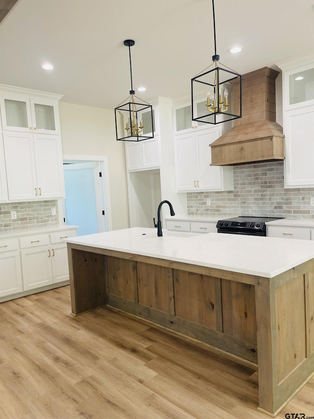 kitchen featuring a center island with sink, white cabinetry, light hardwood / wood-style flooring, pendant lighting, and electric range