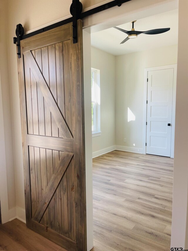 interior space with ceiling fan, a barn door, and light hardwood / wood-style floors