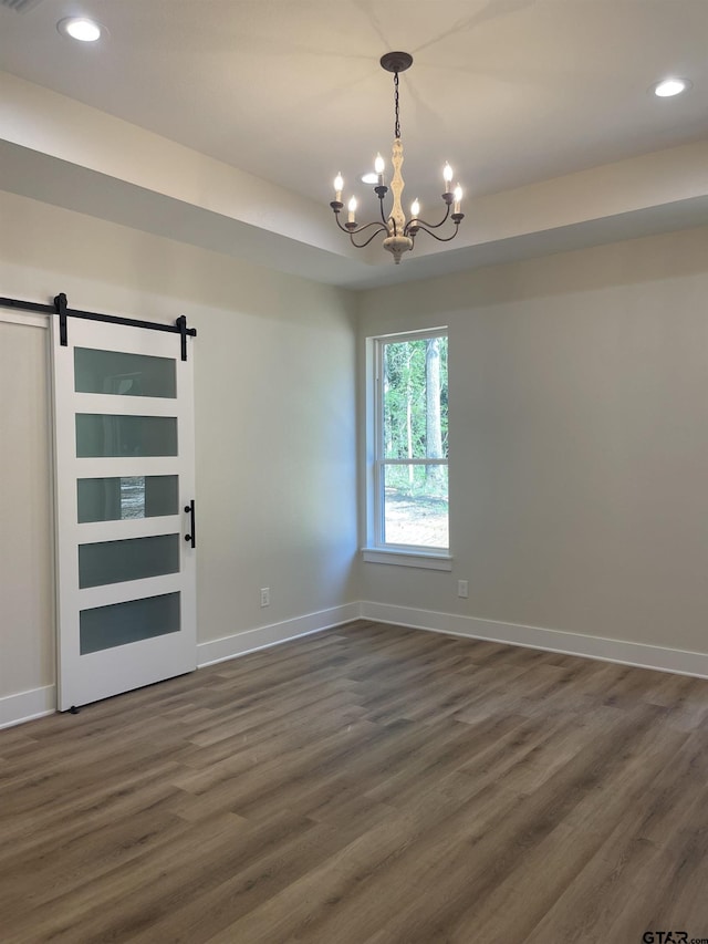 unfurnished room featuring dark wood-type flooring, a barn door, and an inviting chandelier