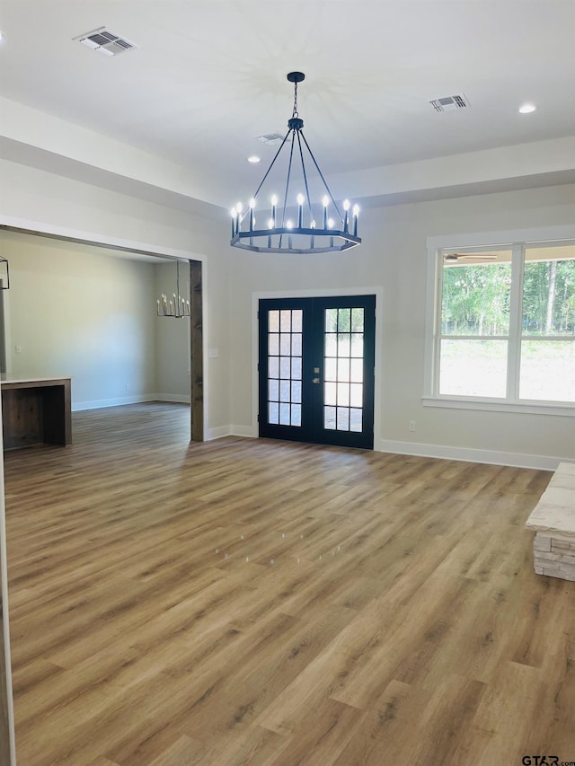 unfurnished dining area with wood-type flooring, a chandelier, and french doors