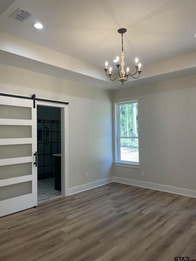 unfurnished room with dark wood-type flooring, a chandelier, and a barn door