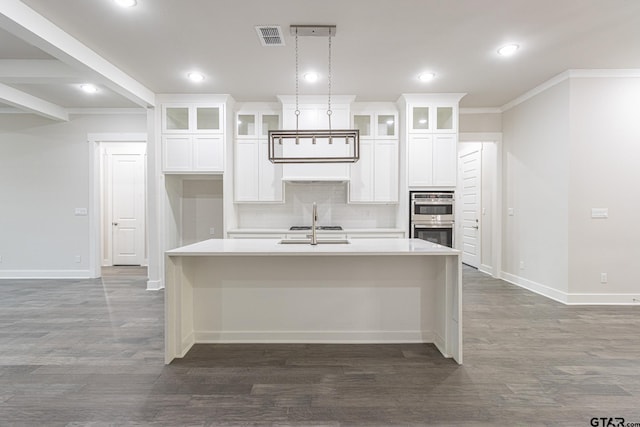 kitchen with white cabinetry, double oven, a kitchen island with sink, and tasteful backsplash