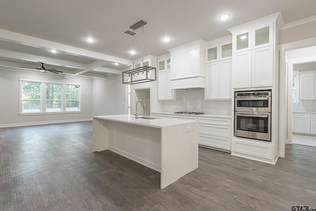 kitchen with decorative light fixtures, beamed ceiling, sink, stainless steel appliances, and a center island with sink