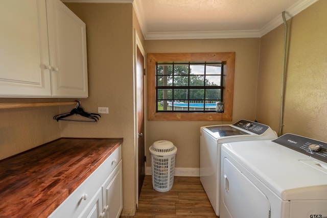 clothes washing area with ornamental molding, hardwood / wood-style flooring, cabinets, and washer and dryer