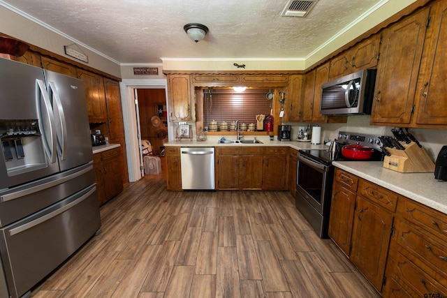 kitchen featuring stainless steel appliances, sink, a textured ceiling, wood-type flooring, and crown molding