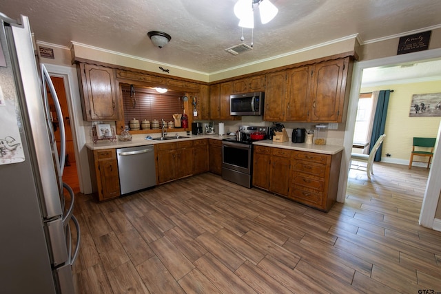 kitchen featuring ornamental molding, appliances with stainless steel finishes, a textured ceiling, sink, and hardwood / wood-style flooring